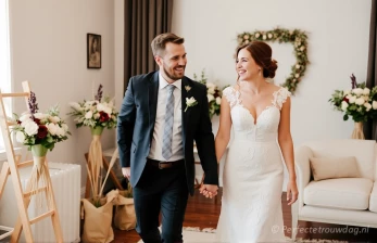 Stel loopt hand in hand bij de trouwlocatie met veel decoratie in de ruimte.